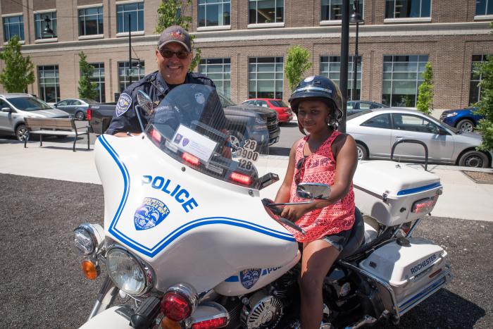 A photo of a girl on a police motorcycle with an officer next to her.