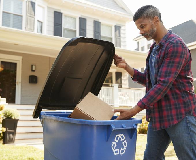 Photo of a man putting cardboard in a recycling bin.