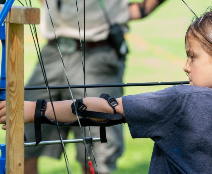 A photo of a girl aiming a bow at an archery camp.