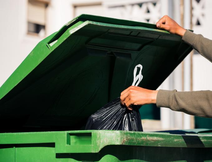 Photo of a person putting a gargbage bag into a dumpster.