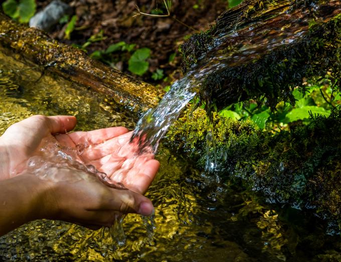 Photo of human hands under a natural spring.