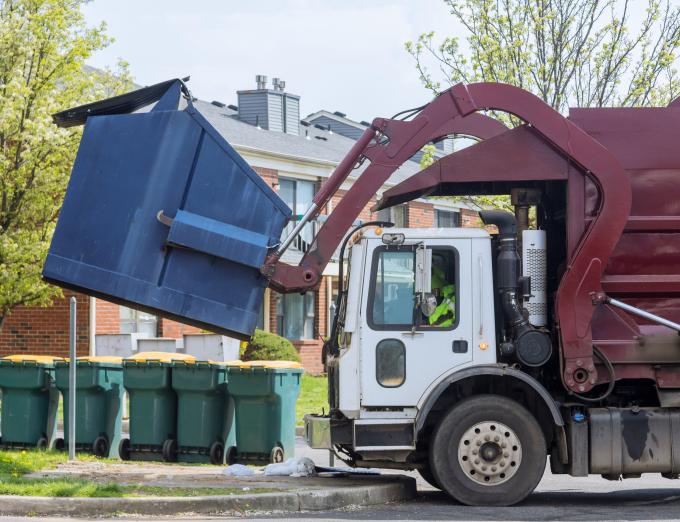 Photo of a garbage truck lifitng a dumpster.