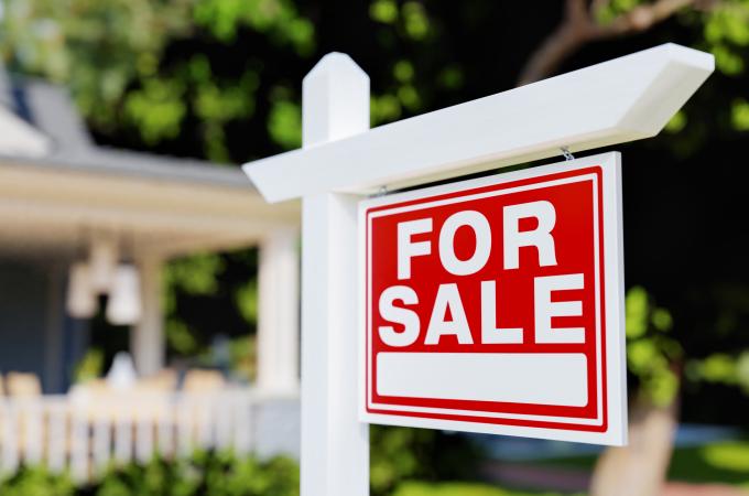 Photo of a for sale sign outside of a house.