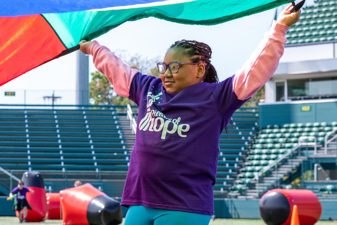 Young girl in a Pillars of Hope t-shirt participating in a parachute activity